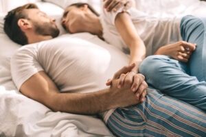 Man and women laying together in bed holding hands.